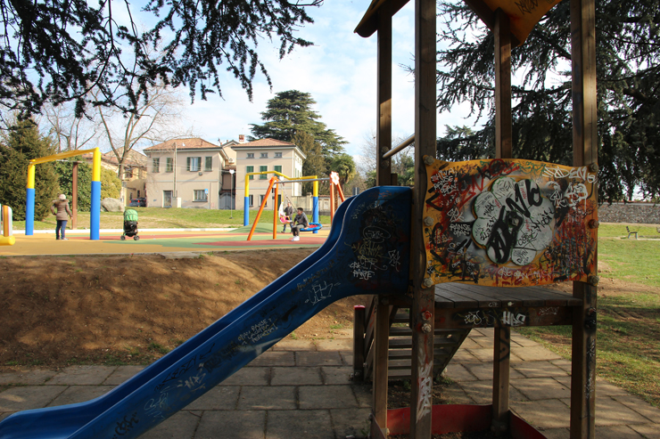 Sullo sfondo del nuovo parco giochi, una delle vecchie installazioni, ricoperta di scritte e graffiti.